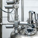 Close-up of stainless steel machinery and pipes in an industrial setting, showcasing modern engineering.