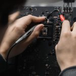 Close-up of hands repairing a circuit board using a soldering iron, emphasizing technical skill.