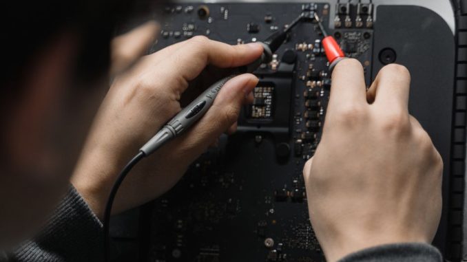 Close-up of hands repairing a circuit board using a soldering iron, emphasizing technical skill.